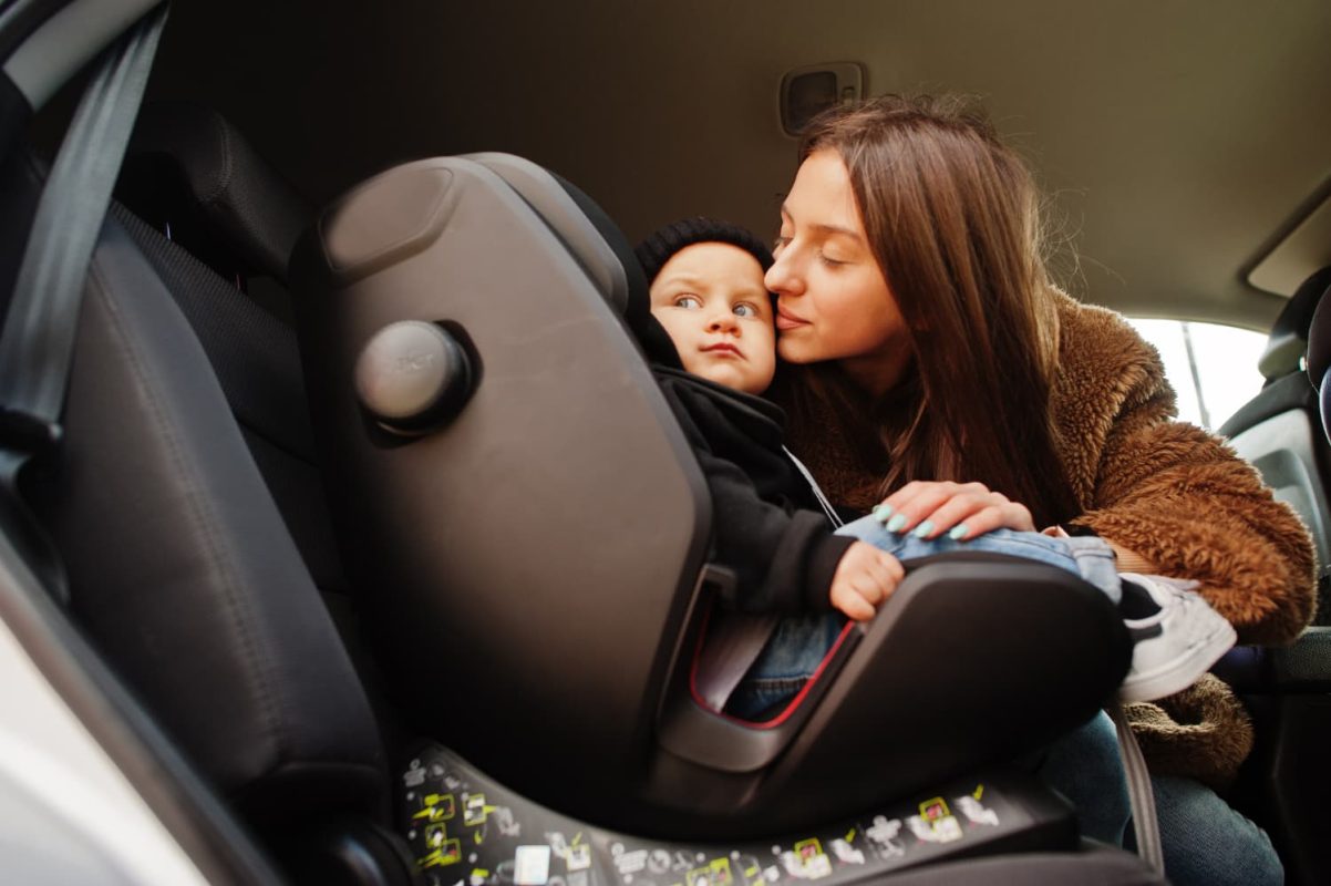 mother kissing baby in baby car seat